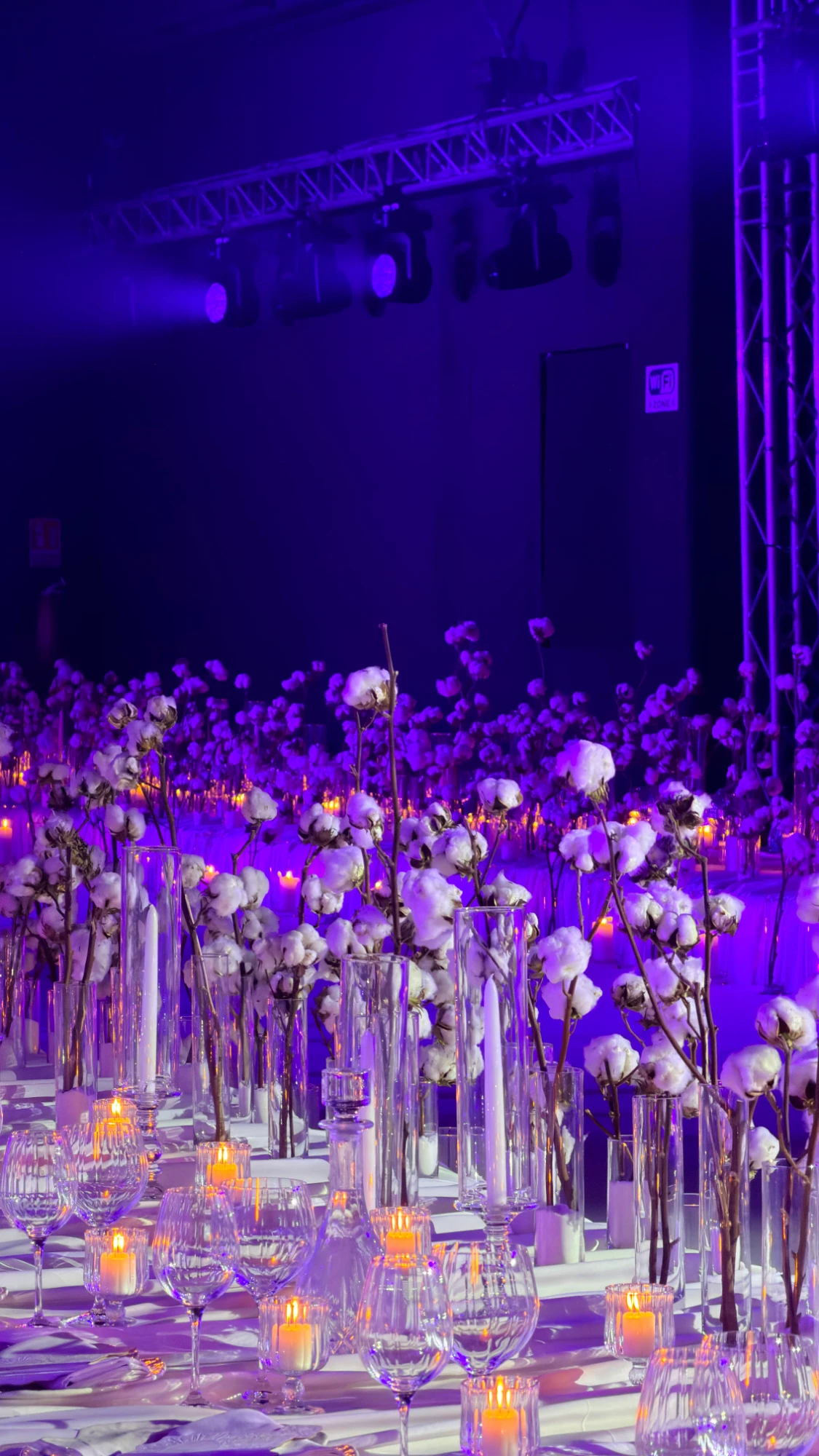 Table at a wedding reception with ornamental cotton branches, candles and stemmed glasses